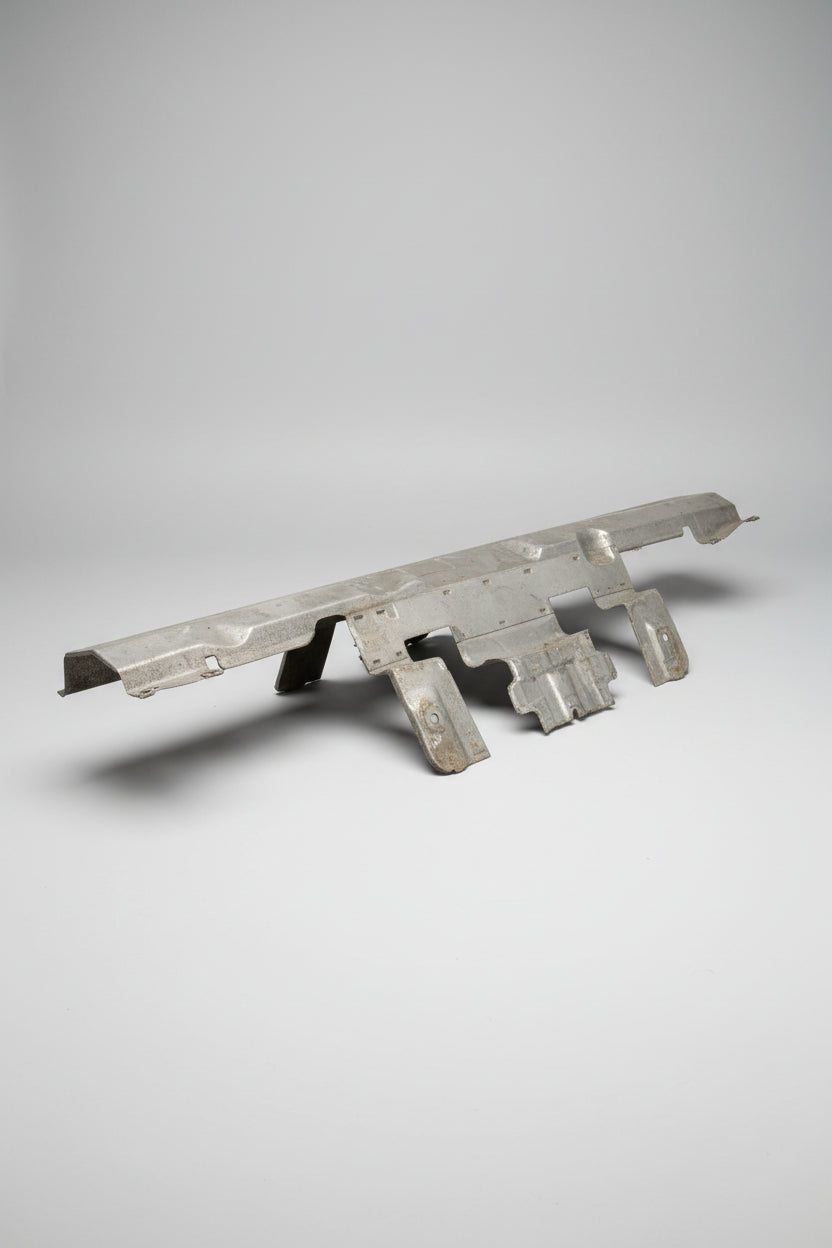 A used, unpainted metal automotive body panel or trim piece with mounting holes, resting on a blue surface inside a cluttered garage or workshop.